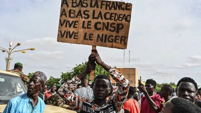 쿠데타 지지자들이 프랑스와 지역 기구 에코와스를 비난하는 표지판을 들고 있다