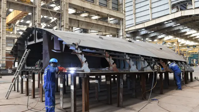 ভারতের গুজরাটে রিলায়েন্স নে।ভাল অ্যান্ড ইঞ্জিনিয়ারিং লিমিটেডের জাহাজ নির্মাণের ঘাটে কর্মরত কয়েকজন শ্রমিক।