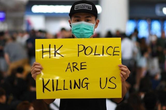 香港国际机场一号客运大楼内一名示威者举着“香港警察在杀害我们”标语牌（12/8/2019）