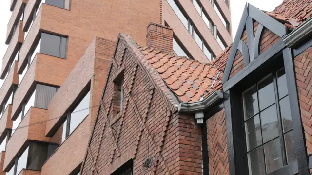 Casa estilo inglés y edificio contemporáneo detrás, ambos con ladrillo a la vista.