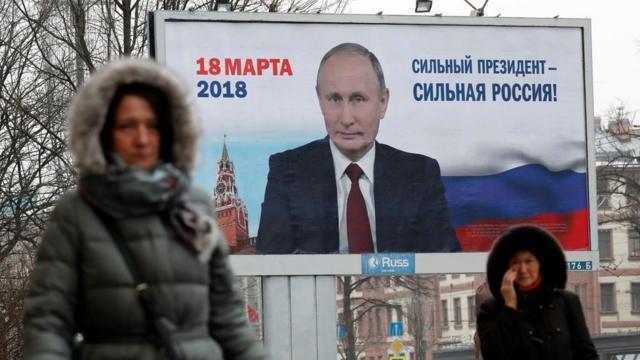 Women pass a Putin election poster in St Petersburg, Russia, 12 January