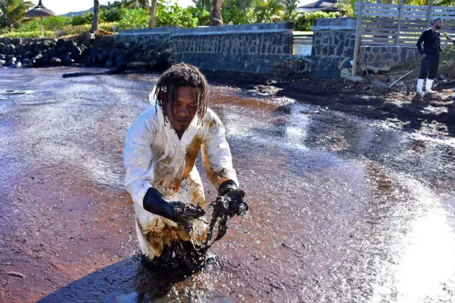 A volunteer stands in the sludge which he handles with gloved hands.