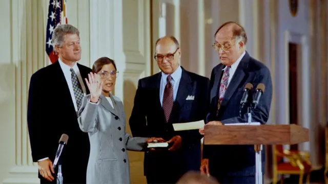 Justiça Ginsburg é empossada na Suprema Corte americana, com seu marido Martin segurando a bíblia. O então presidente Bill Clinton acompanha a cerimônia próximo ao casal.