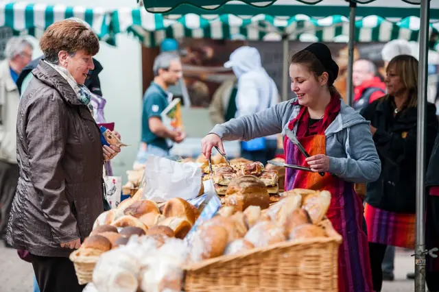 Mujer vende repostería en un mercado de agricultores de Pembrokeshire, Gales.