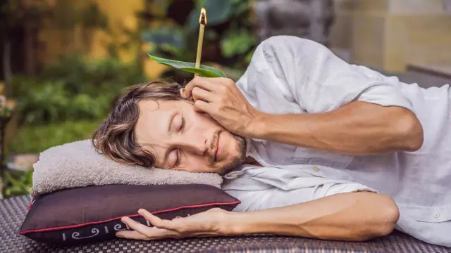 Homem com vela no ouvido, deitadocomo jogar na esporte betmeio a jardim