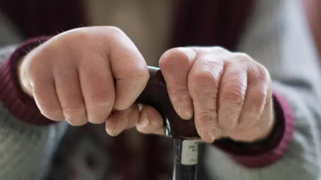 مسن يمسك عصا بيديه