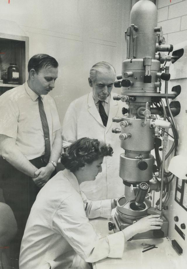阿尔梅达在操作显微镜，识别和拍摄病毒颗粒图像。身后是唐纳德·帕森斯博士（Dr. Donald Parsons，左）和亚瑟·W.H.博士（Dr. Arthur W.H.）