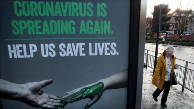 One woman wey wear face mask waka pass coronavirus poster for Glasgow