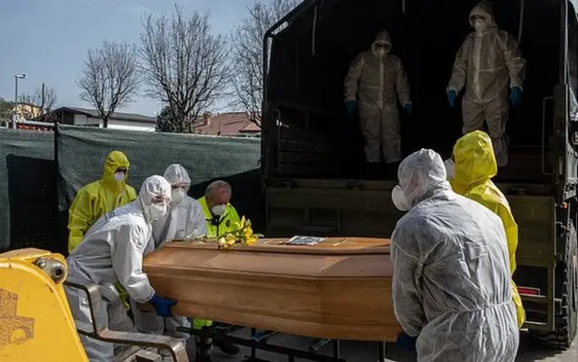 Carabinieri officers, wearing protective suits, lift a coffin on March 28, 2020 in Ponte San Pietro, near Bergamo