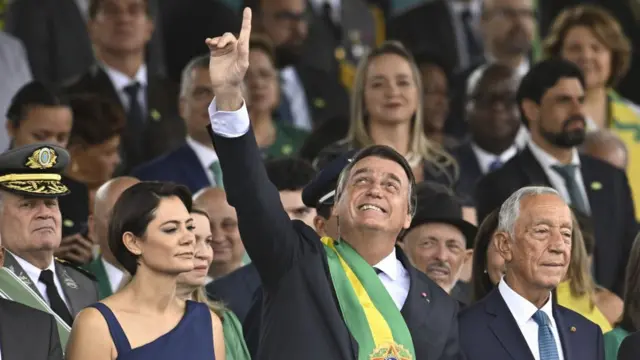 Presidente Jair Bolsonaro ao centro, com o braço apontado para o céu, acompanhado da primeira-dama e do presidenteestrategia para jogar roletaPortugal