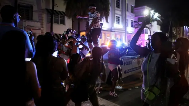 Un hombre baila arriba de un auto rodeado de una multitud en Miami Beach.