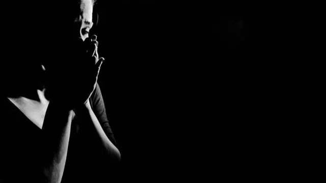 Mujer que se toma la cara con las manos en medio de sombras.