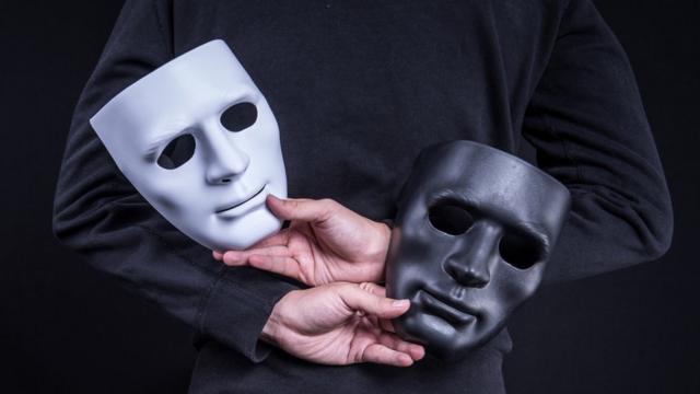 Un hombre sujeta una máscara blanca y otra negra.
