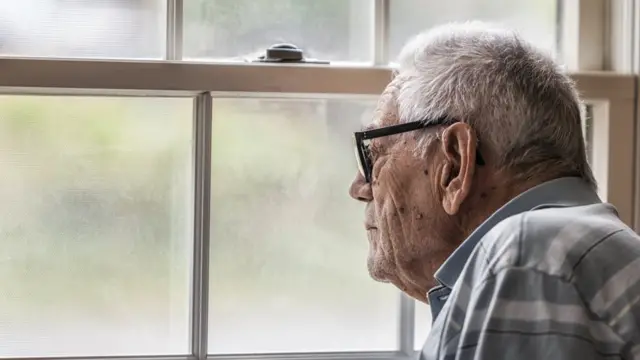 Anciano mirando a través de una ventana.