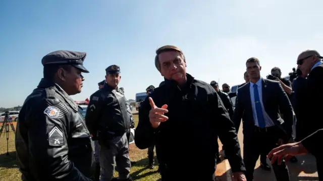 Bolsonaro caminha ao ar livre, rodeado por seguranças