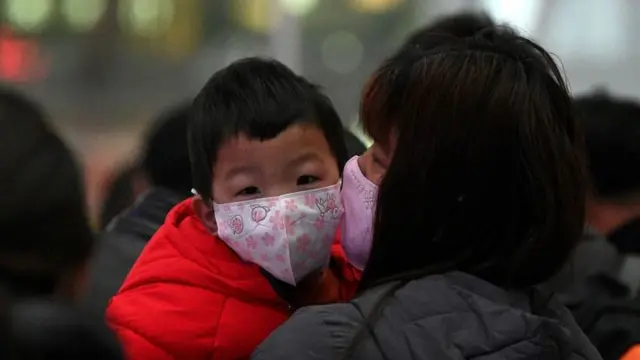 Mujer con un niño en sus brazos, ambos con mascarilla.