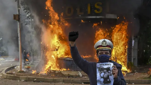 Pengunjuk rasa berfoto dengan latar belakang api yang membakar pos polisi saat demonstrasi menentang UU Cipta Kerja di kawasan Patung Kuda, Jakarta, Kamis (08/10)