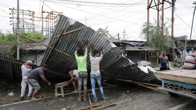 Hombres levantan chapas volcadas por el ciclón en Bokkhali, India.