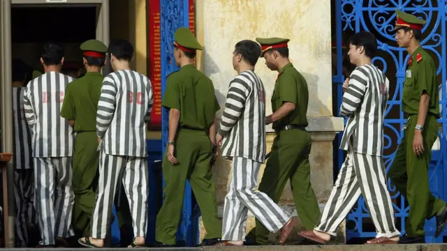 Escorted defendants walk through a security-check gate into the Ho Chi Minh-City court house for the final verdict of the country's biggest evert corruption scandal 04 June 2003.