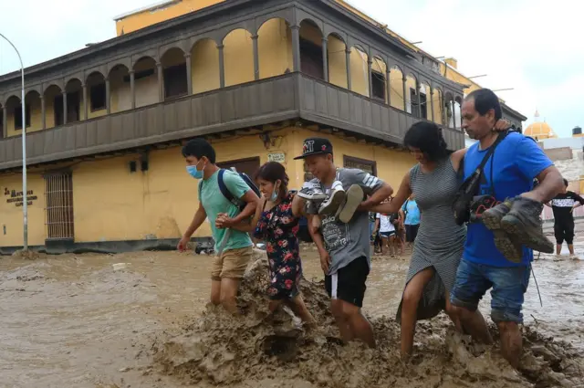 Personas tratando de cruzar una calle en medio del lodo.
