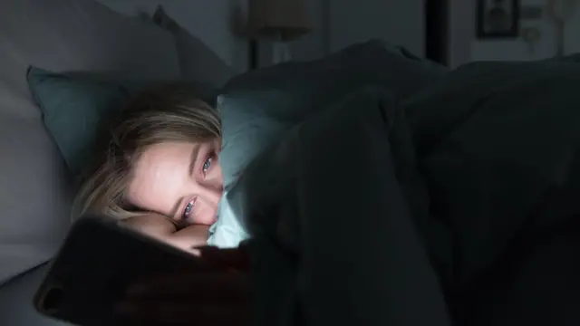 Una mujer en la cama iluminada con el teléfono.