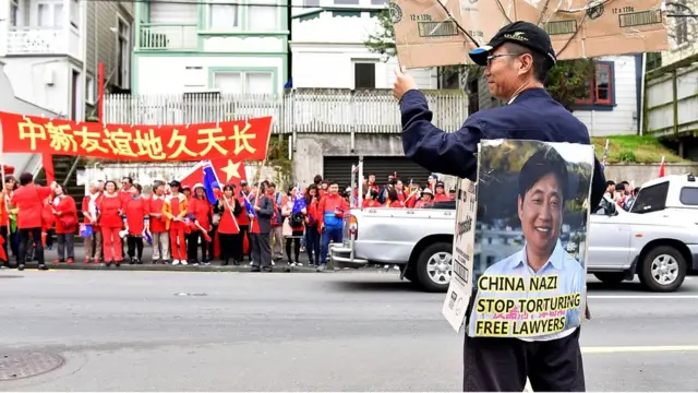 A protester holds a sign opposite Chinese supporters outside Premier House after China's Premier Li Keqiang left a press conference in Wellington on March 27, 2017.