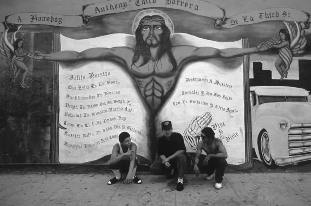 Трое мужчин сидят на фоне настенного рисунка с изображением Христа