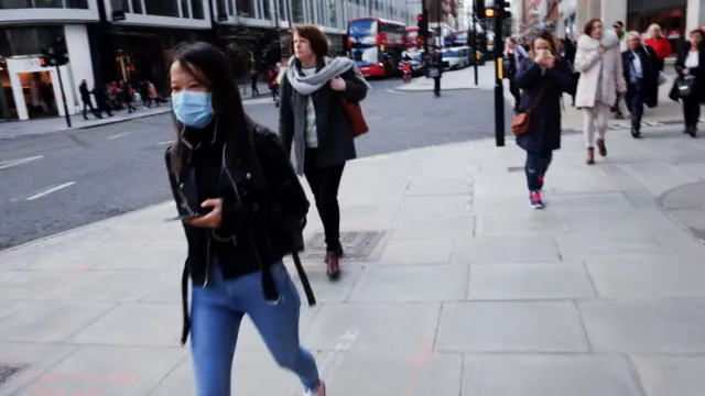 Pessoas andando numa calçada, algumas com mascara