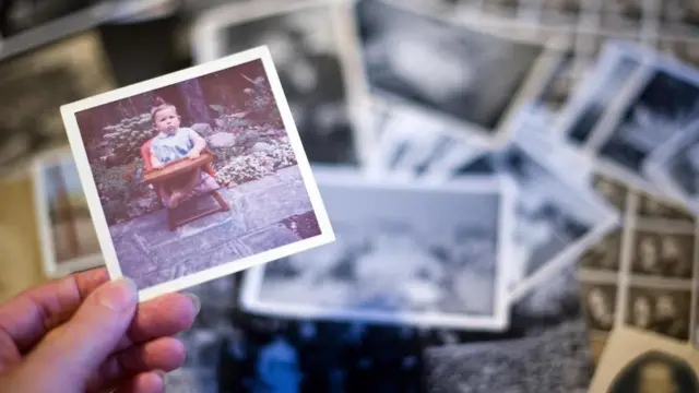 Una persona sosteniendo una fotografía en la mano, de una pila en una mesa