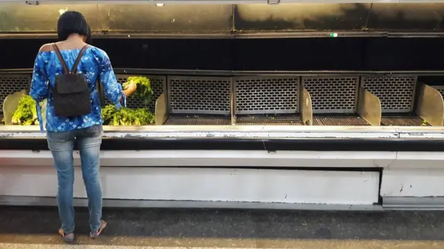 Mujer buscando vegetales en anaqueles casi vacíos en Caracas, Venezuela.