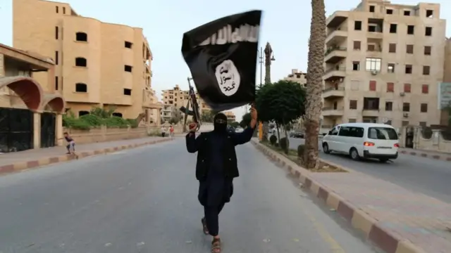 Naoručani pripadnik Islamske države nosi zastavu u ruci u Raki u junu 2014. godine