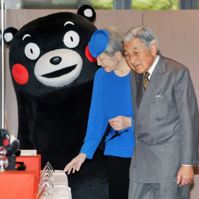 Japanese Emperor Akihito (R) and Empress Michiko (C) stand next to 'Kumamon' (L)