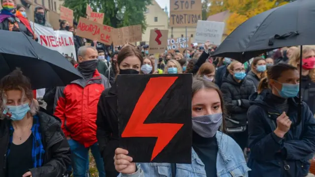 A protester wearing a face mask holds a placard expressing her opinion during the demonstration