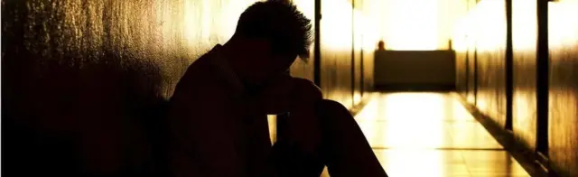 Wani mutum a zaune ya haɗa kai da gwiwa