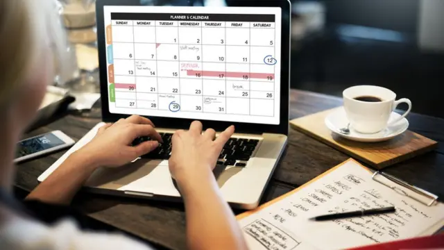 Una mujer escribe en un calendario en su computadora.