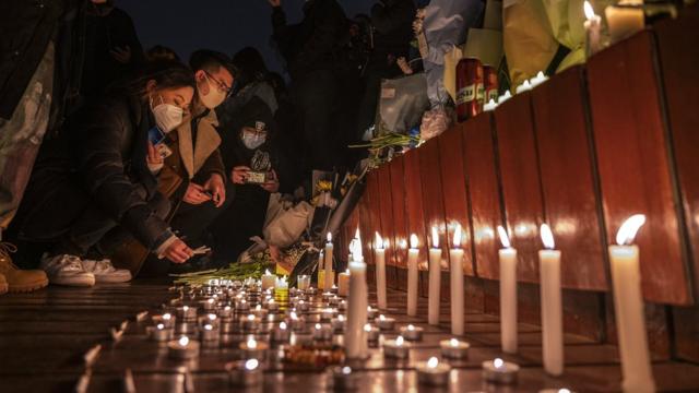 2022年11月27日,北京抗议者在为乌鲁木齐公寓火灾的遇难者举行的悼念活动上点燃蜡烛并留下香烟。