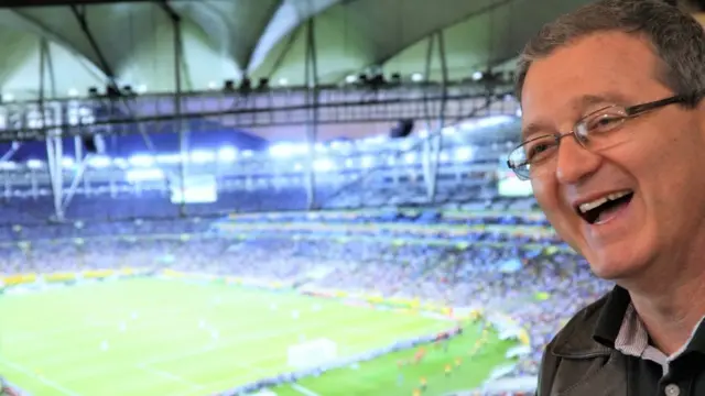 O rosto do estatístico Francisco Louzada (à direita); ao fundo, um estádio lotado.