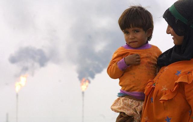 سيدة عراقية تحمل طفلها وفي الخلفية حقوق النفط العراقية.