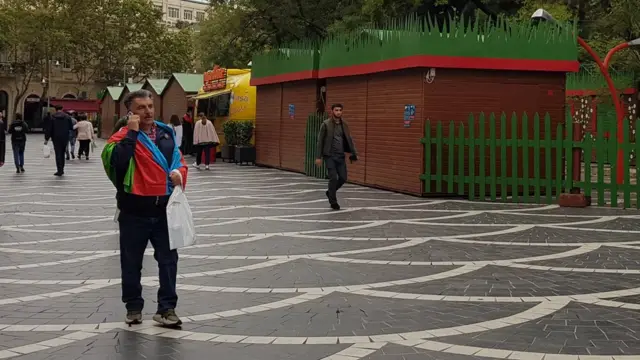 Мужчина завернутый флаг на фоне киосков.