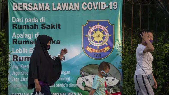 Sejumlah warga dengan mengenakan masker berjalan dengan latar belakang spanduk peringatan bahaya COVID-19 di Sunter, Jakarta, Sabtu (22/8/2020)