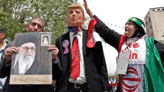 Демонстрация протеста в Иране - протестующий держит фотографию аятоллы Хаменеи, рядом фигура Трампа