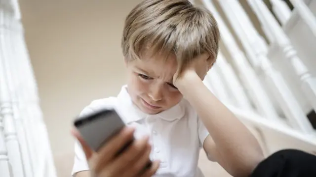 niño mirando celular con gesto de preocupación