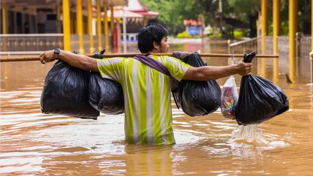 थाईल्यान्डमा भारी बोकेर जलमग्न सडक पार गर्दै एक मानिस