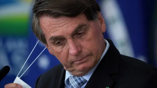 Le président brésilien Jair Bolsonaro enlève son masque lors de la cérémonie de signature des projets de loi visant à élargir la capacité d'achat de vaccins par le gouvernement fédéral, au palais du Planalto, à Brasilia, au Brésil, le 10 mars 2020.