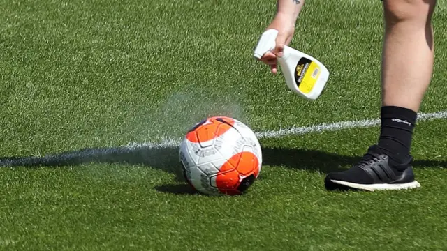 A member of staff sprays a ball with disinfectant