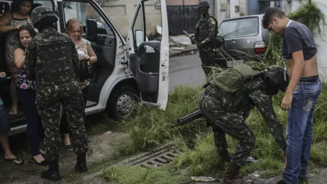 Soldados revistam homem na rua