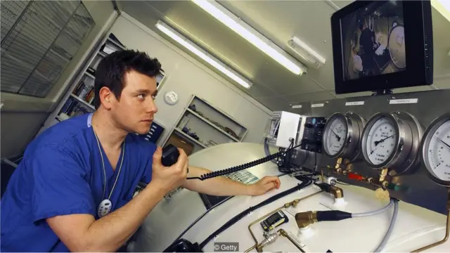 Seorang teknisi berkomunikasi dengan penyelam di ruangan hiperbarik.