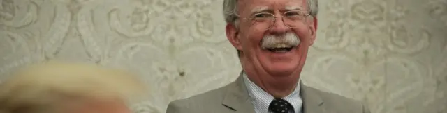President Donald Trump speaks to members of the media as National Security Adviser John Bolton listens during a meeting with President of Romania Klaus Iohannis in the Oval Office of the White House August 20, 2019
