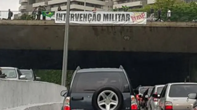 Carro na rua e ponte com faixa pedindo intervenção