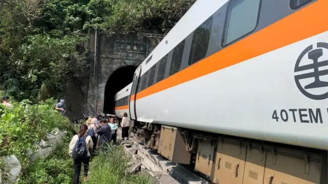 People walk next to a train which derailed in a tunnel north of Hualien